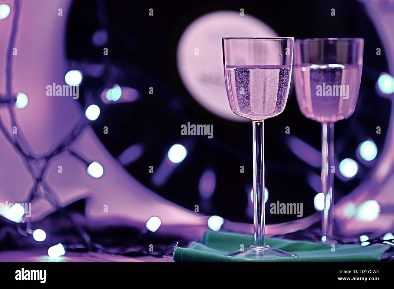 Selektiver Fokus Foto von zwei Gläsern Champagner auf dem Hintergrund einer Vinyl-Platte, umgeben von hellen Club Beleuchtung Stockfoto