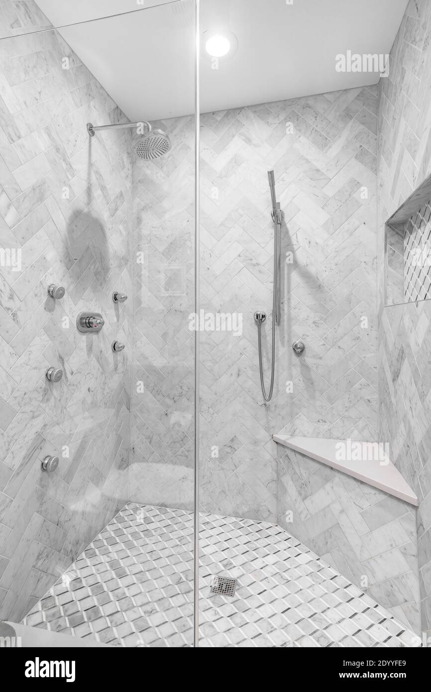 Eine luxuriöse renovierte Dusche mit Marmorfliesen, eine Sitzbank und Chrom-Armaturen. Die Wände sind mit Fischgrätmuster bedeckt. Stockfoto