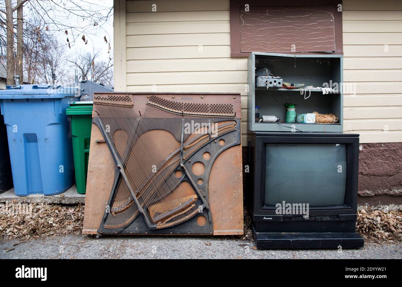 Ein altes Klavier-Soundboard, Elektronik und ein Fernseher in der Gasse warten auf Müll, Abfallbeseitigung und Recycling. Stockfoto