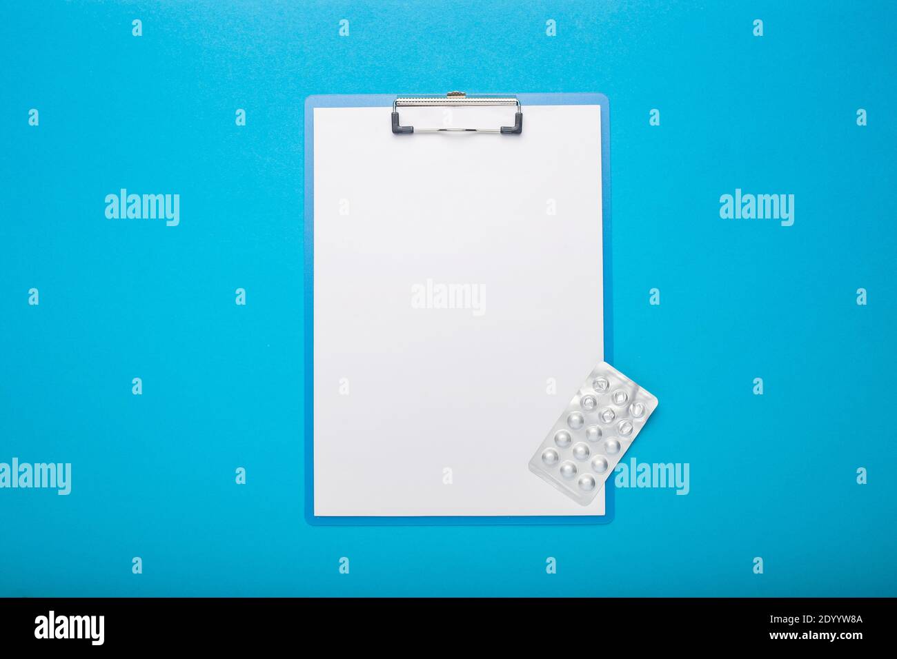 Zwischenablage mit einem leeren Blatt Papier und Pillen auf blauem Hintergrund. Banner. Draufsicht, flach liegend. Stockfoto