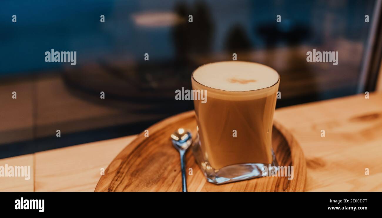 Kaffee Latte mit Schaum und Milch in einem transparenten Glas Steht auf einem Holztablett mit einem Löffel auf dem Tabelle Stockfoto