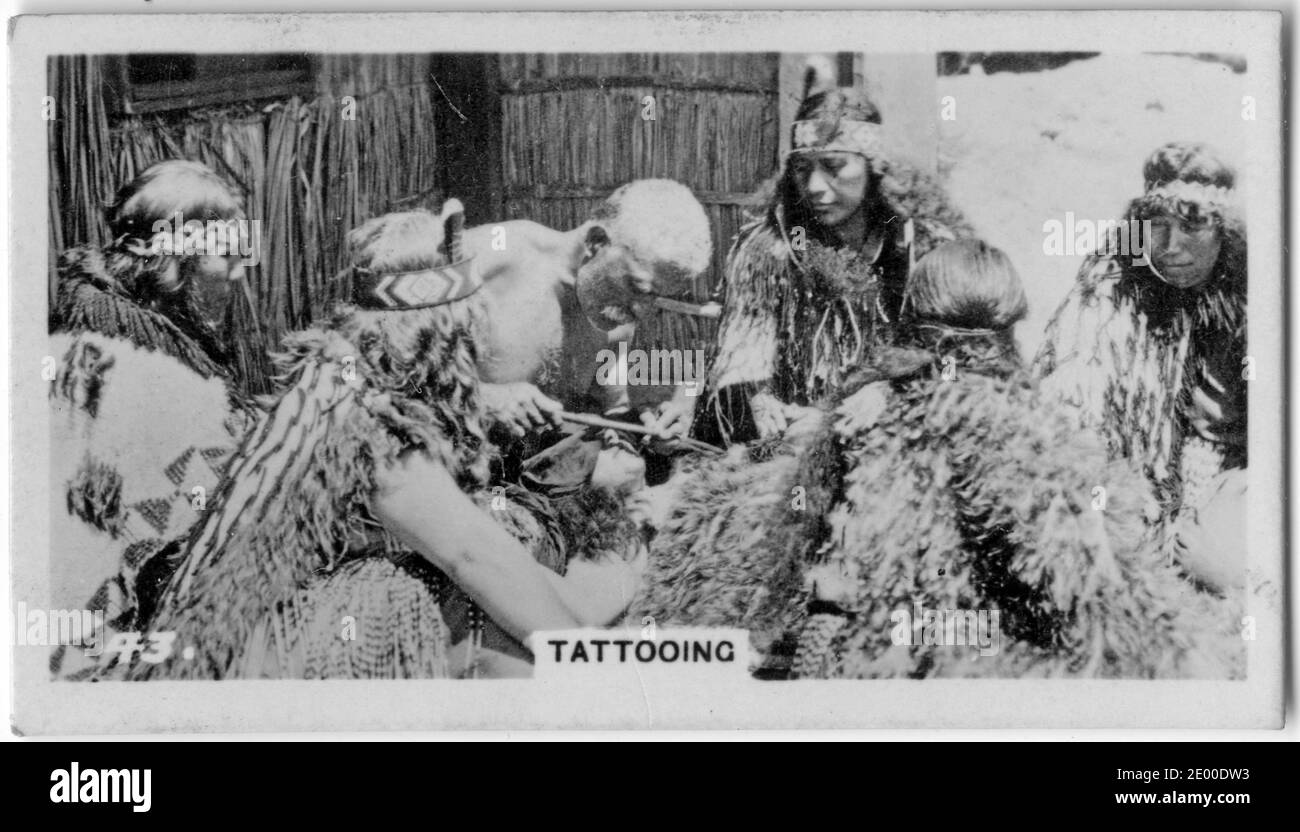 Ein Maori-Ältester, der ein Tattoo tätowiert, während eine Gruppe von Frauen aufpasst, aus einer Zigarettenkarte über die neuseeländische Geschichte, um 1930 Stockfoto