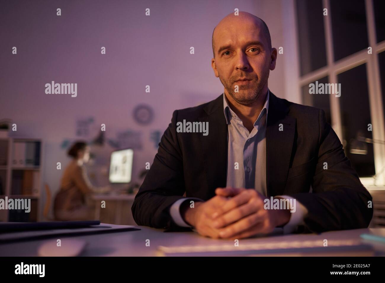 Porträt der modernen kaukasischen Geschäftsperson sitzt am Schreibtisch in Bürozimmer spät am Abend mit Blick auf die Kamera Stockfoto