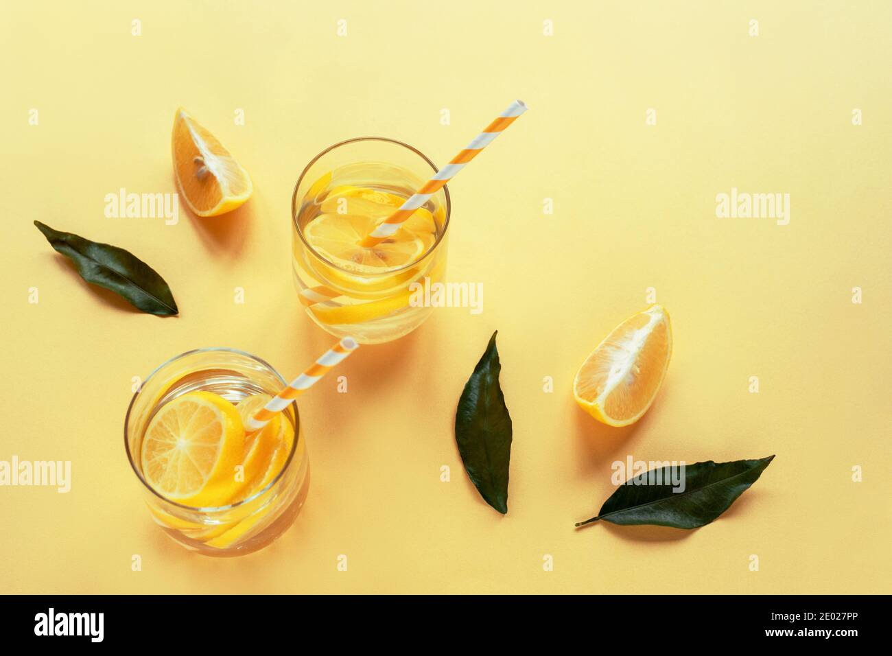 Zwei Gläser mit einer kalten Limonade auf gelbem Hintergrund. Zitronenscheiben und grüne Blätter. Kühlender Drink im Sommer. Draufsicht. Stockfoto