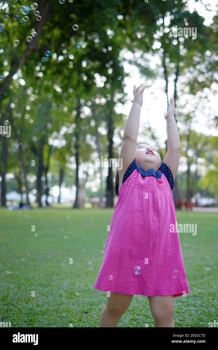 Ein süßes asiatisches Mädchen, das mit Blasen auf einem Rasen in einem Park in Thailand spielt. Stockfoto