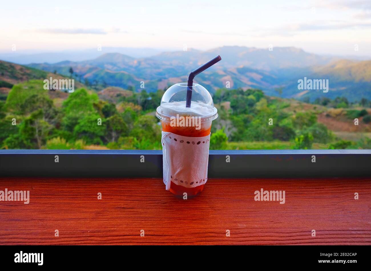 Eine kalte Tasse Eistee auf einem Tisch mit Blick auf eine wunderschöne Bergkette und schönen klaren Himmel im Norden Thailands. Stockfoto