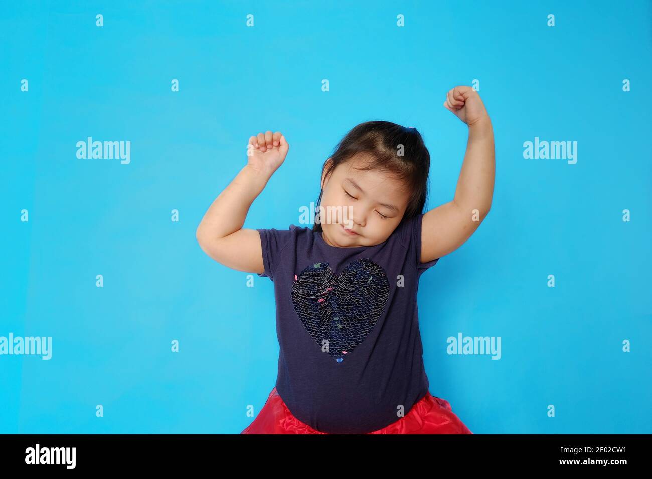 Ein nettes weibliches asiatisches Kleinkind, das Spaß hat und zum Rhythmus der Musik tanzt. Einfacher hellblauer Hintergrund. Stockfoto