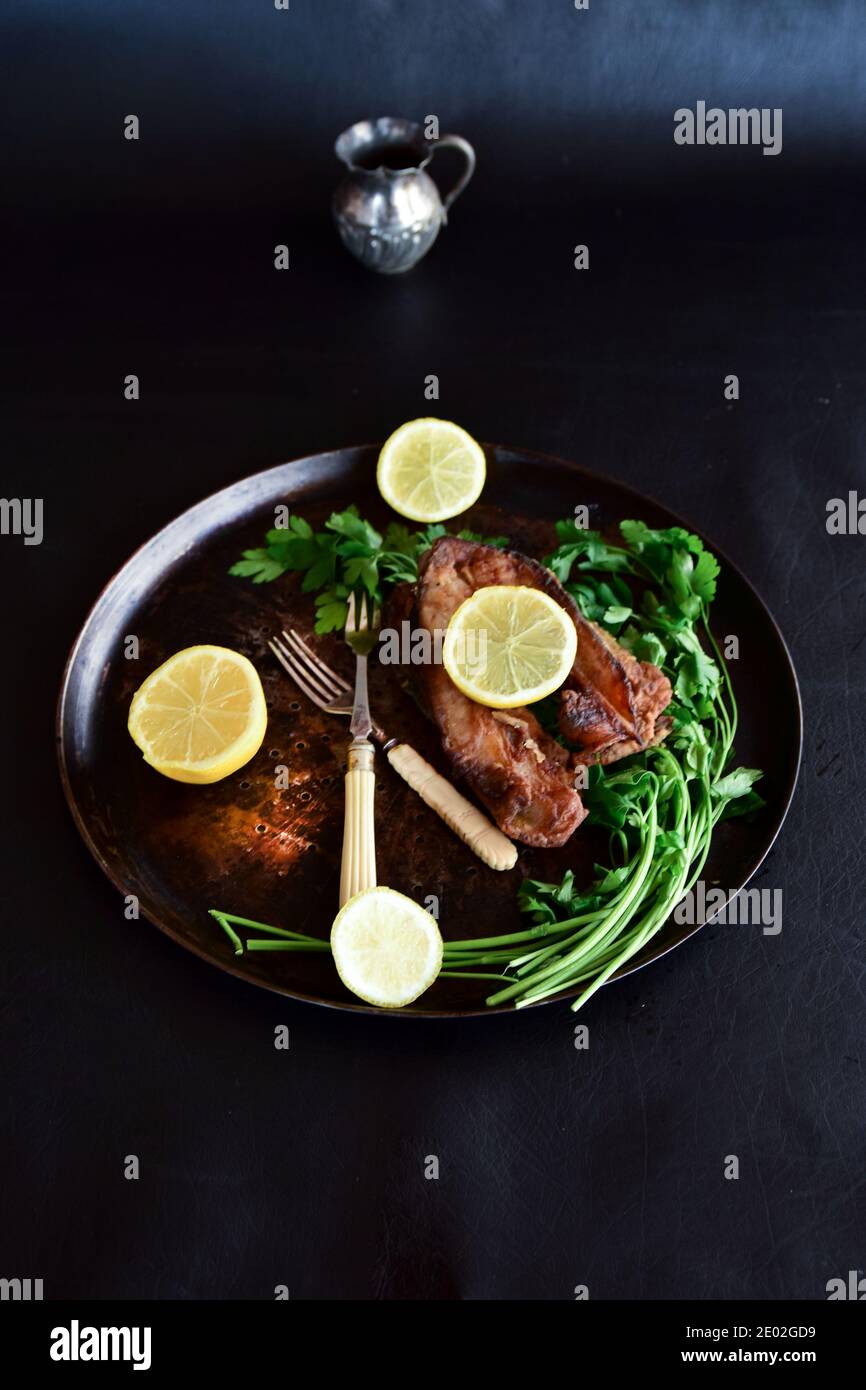 Gebratener Karpfen mit Zitrone und grüner Petersilie auf schwarzem Hintergrund. Traditionelles polnisches Gericht für Heiligabend. Stockfoto