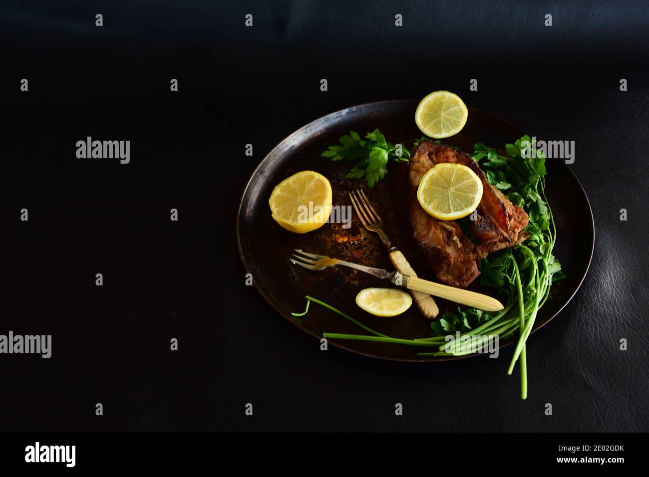 Gebratener Karpfen mit Zitrone und grüner Petersilie auf schwarzem Hintergrund. Traditionelles polnisches Gericht für Heiligabend. Stockfoto