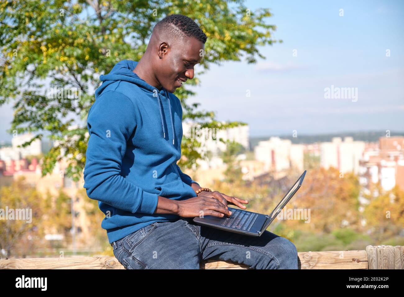 Afrikanischer schwarzer Mann lächelt und arbeitet mit einem Laptop in einem Park. Digital Nomad Entrepreneur Konzept. Stockfoto