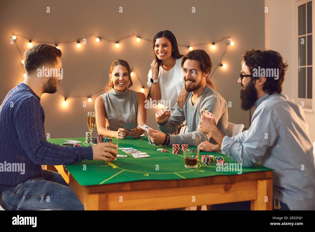 Fröhliche Gesellschaft von männlichen und weiblichen Freunden, die an einem Pokertisch sitzen und den Abend genießen. Stockfoto