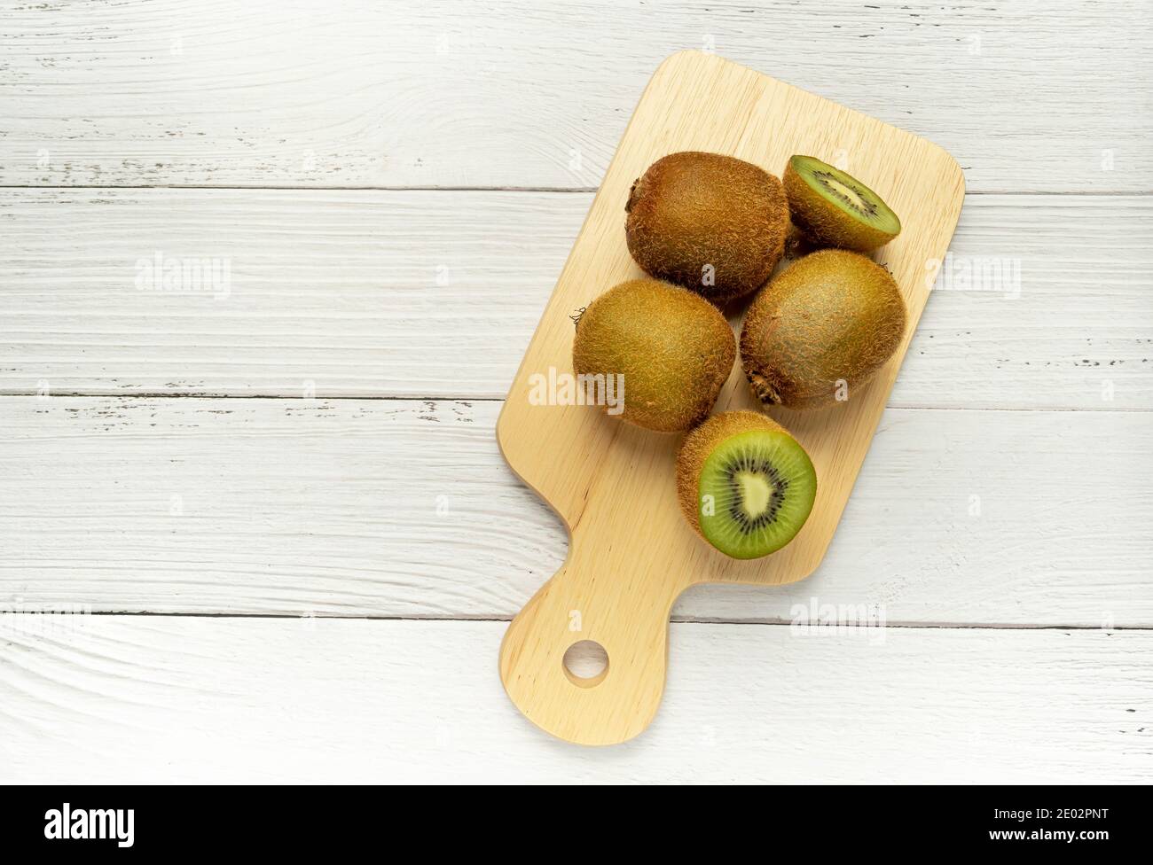 Reife ganze Kiwi-Früchte und halbe Kiwi-Früchte auf Holzschneidebrett. Volle Tiefe des Feldes. Veganes Lebensmittelkonzept Stockfoto