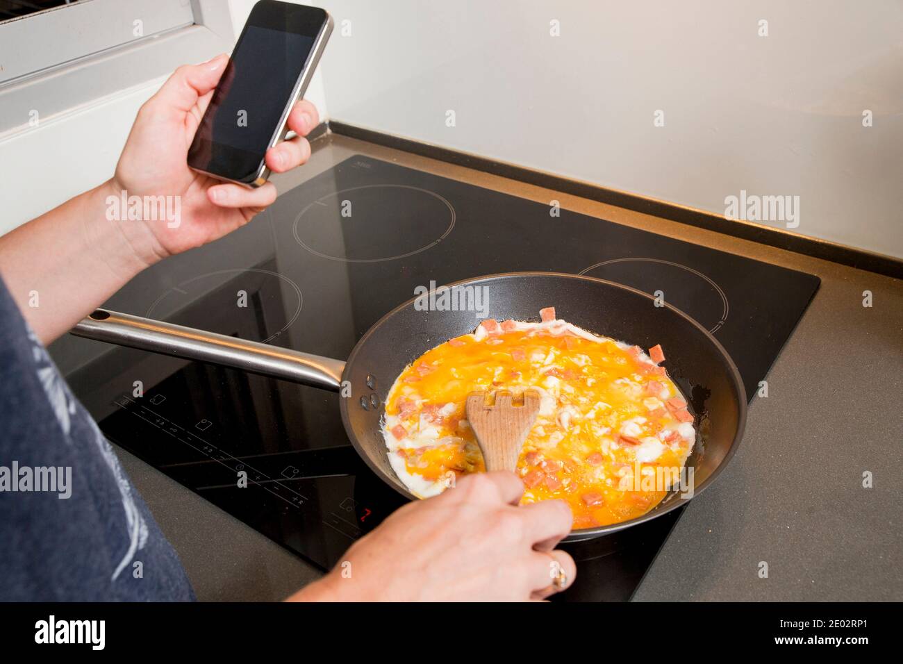 Hausarbeit. Frau kocht, während sie ihr Smartphone zur Kommunikation und Arbeit nutzt Stockfoto