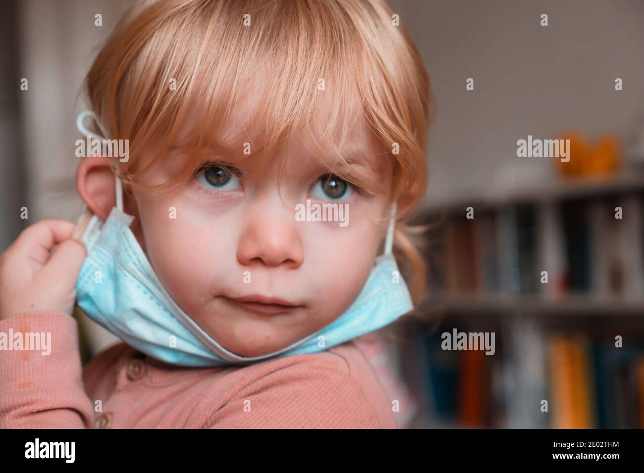 Zwei Jahre altes Kind mit Gesichtsmaske unter dem Kinn zu Hause. Nahaufnahme. Stockfoto