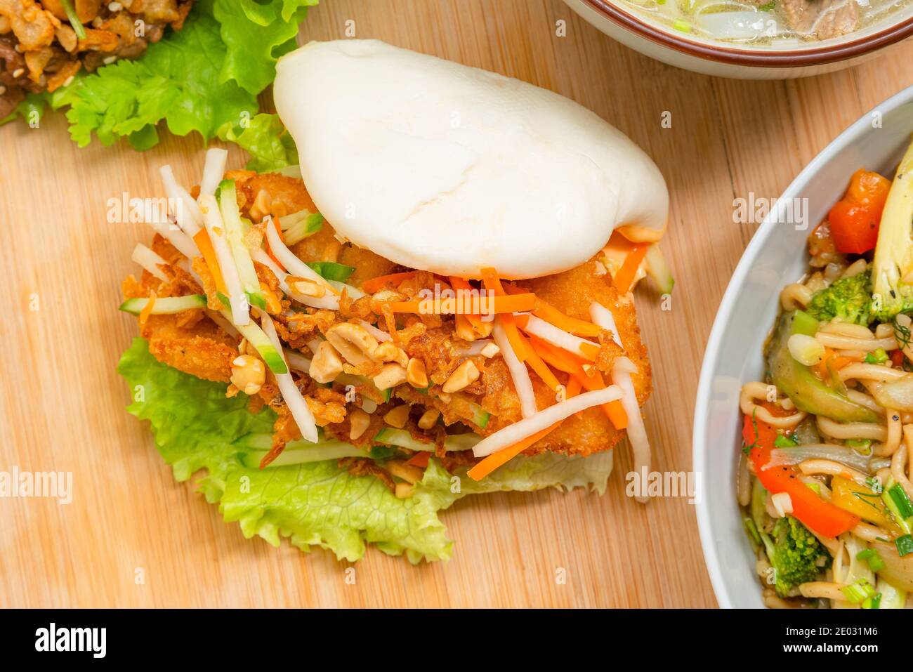 Köstliches gedämpftes bao-Brötchen auf Holztisch mit gebratenem Huhn und frischem Gemüse - Salat, Karotten und gerösteten Erdnüssen. Beliebtes Street Food Stockfoto