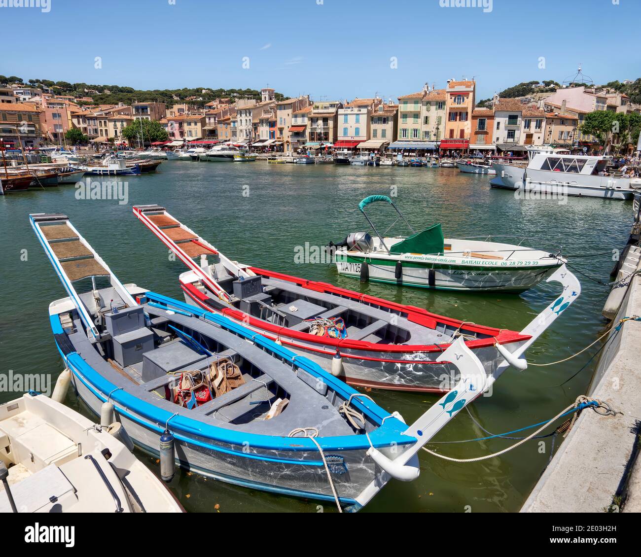 Zwei traditionelle französische Fischerboote, die im Hafen von Cassis, Provence, Frankreich mit Restaurants am Wasser im Hintergrund festgemacht sind Stockfoto
