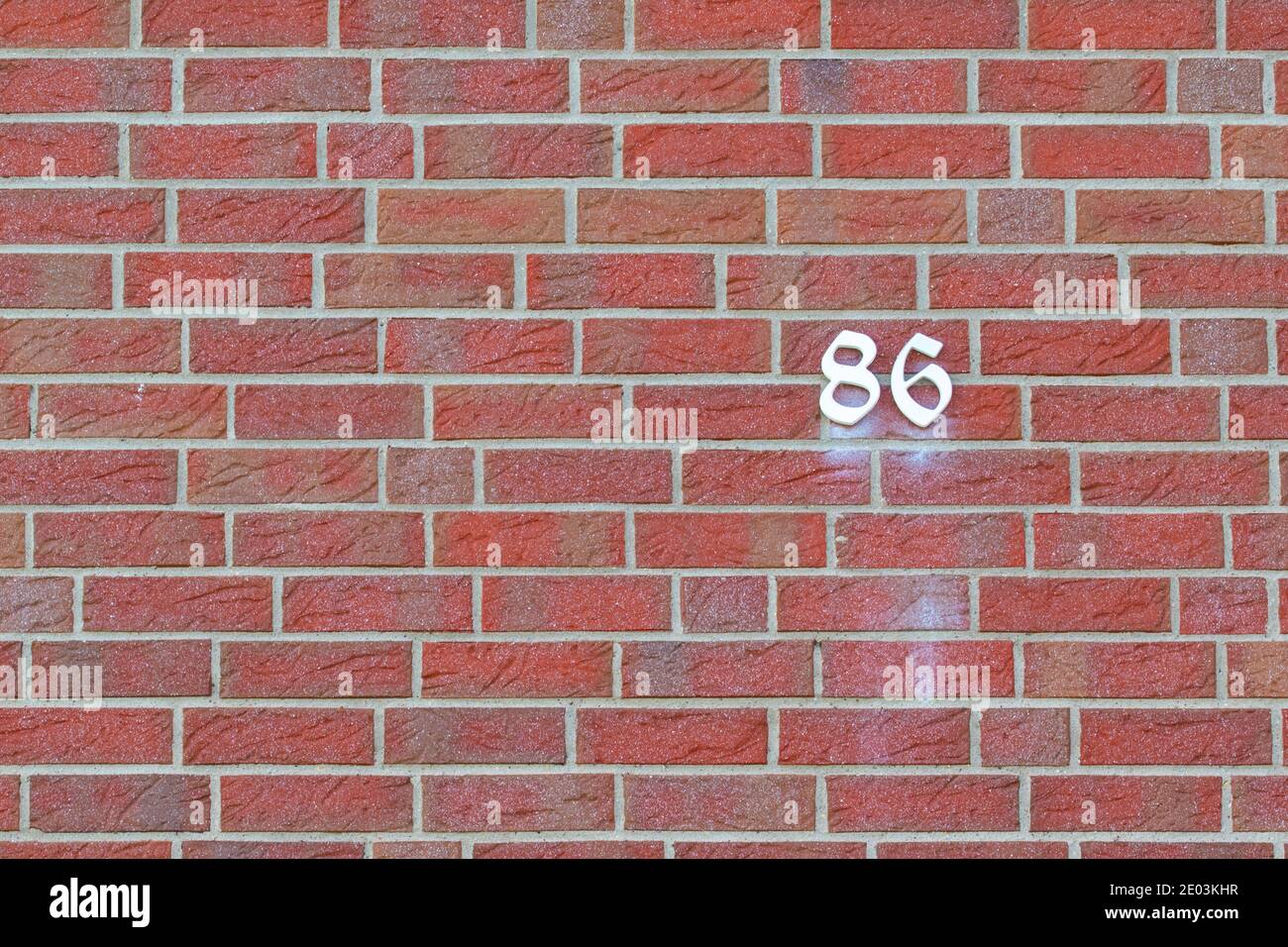 Hausnummer 86 in weiß auf einer roten Backsteinmauer geschrieben. Stockfoto