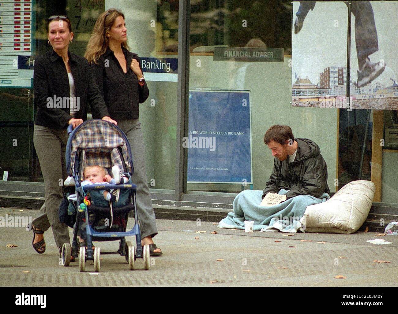 Reiche Arme teilen Ungleichheit, obdachlose Bettlerin mit Schlafsack und unterschreiben vor der Barclays Bankfiliale, während Frauen mit ihrem Kind in der Kinderwagen Kings Road Chelsea vorbeigehen Stockfoto Reiche Arme teilen Ungleichheit, obdachlose Bettlerin mit Schlafsack und unterschreiben vor der Barclays Bankfiliale, während Frauen mit ihrem Kind in der Kinderwagen Kings Road Chelsea vorbeigehen Stockfoto