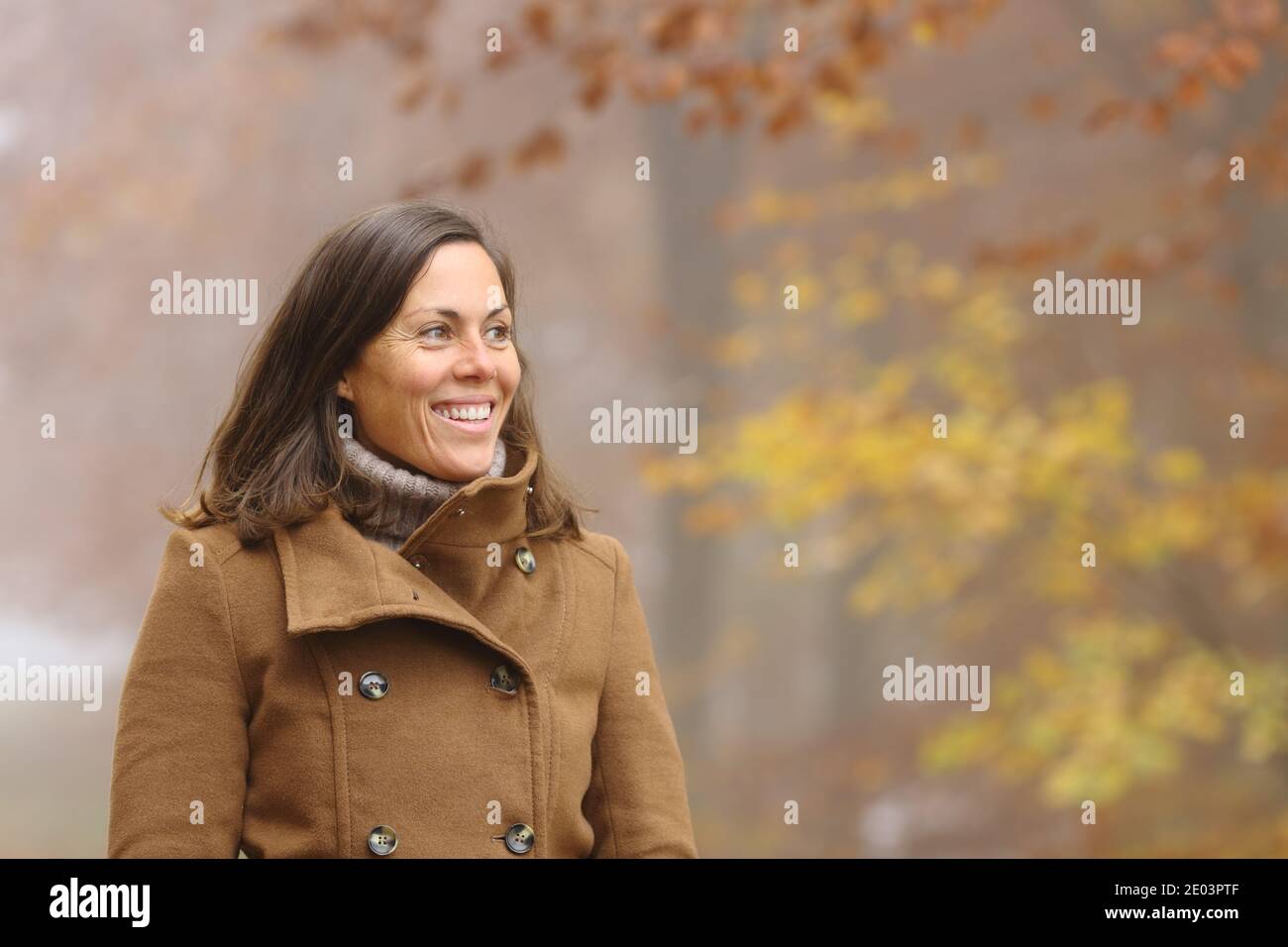 Glückliche Erwachsene Dame, die die Aussicht beim Spaziergang in einem Park in Betracht zieht Herbstsaison Stockfoto