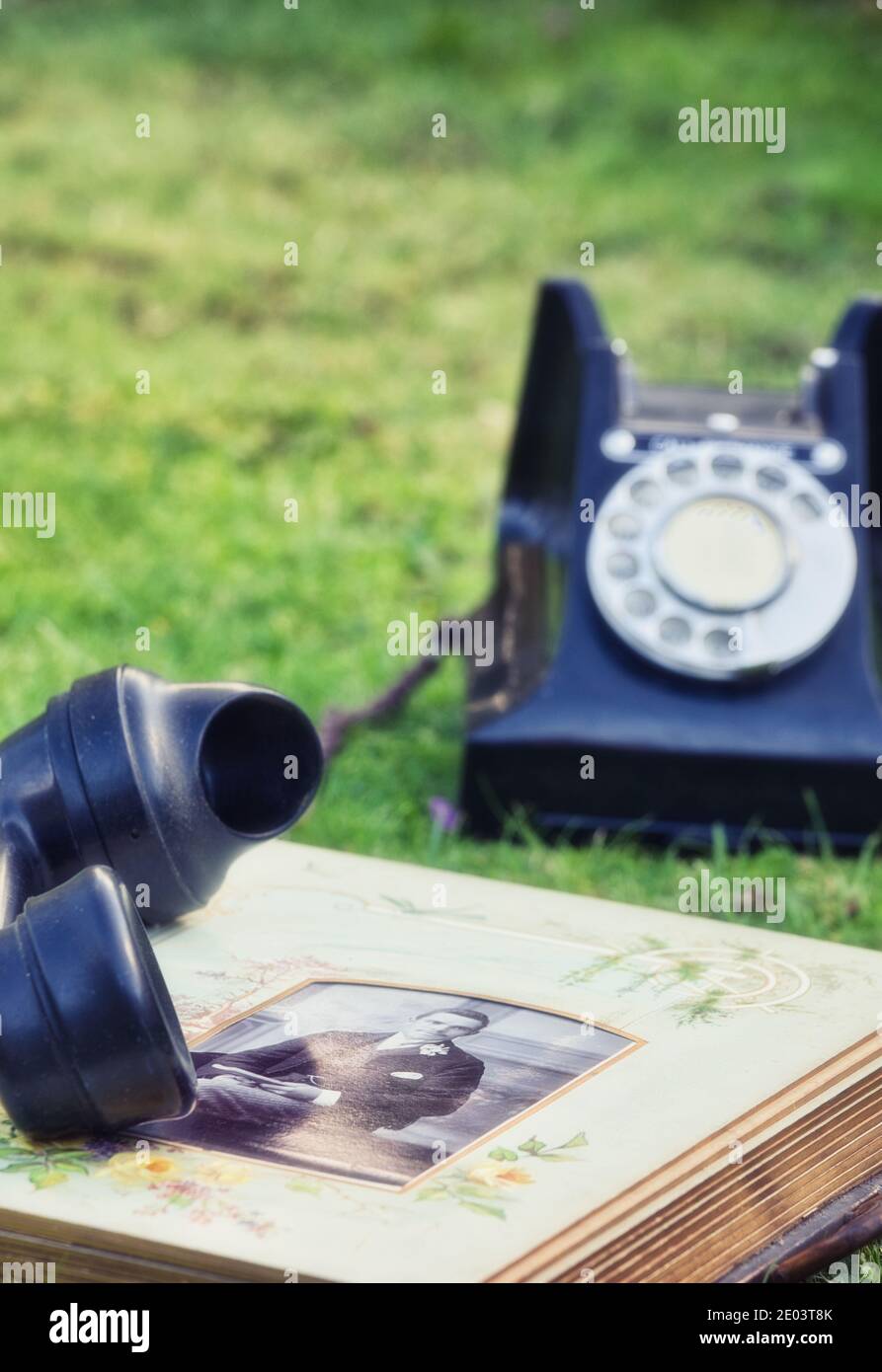 Altes Fotoalbum offen auf Gras mit schwarzem Vintage-Telefon. Konzept der verlorenen Chancen, Erinnerungen, Jahrgang Stockfoto