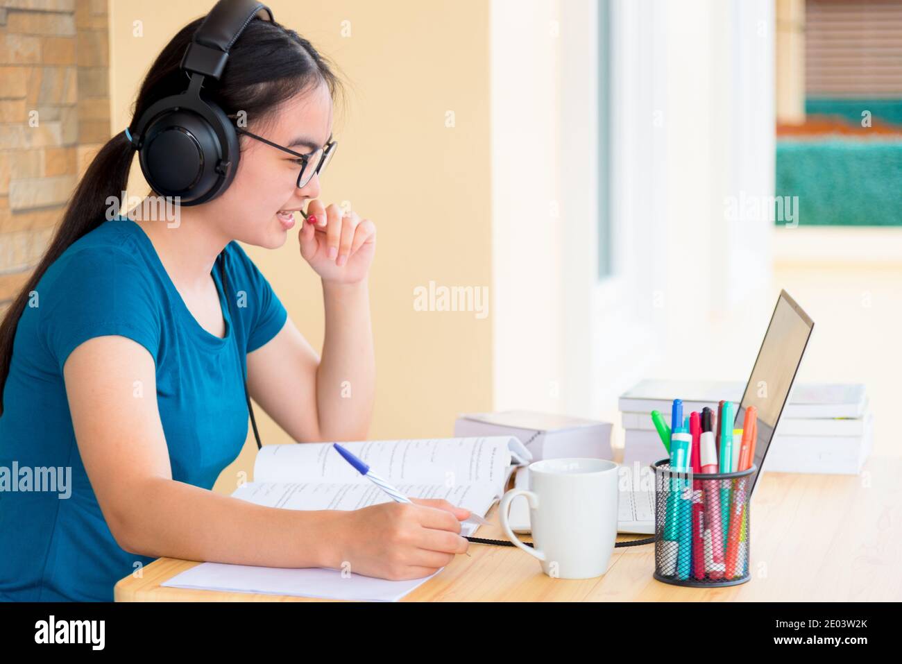 Asiatische Teenager-Studentin mit einem Headset und Brille schaut auf Laptop-Computer online lernen von der Schule und sprechen in ein Mikrofon. Distanz ed Stockfoto
