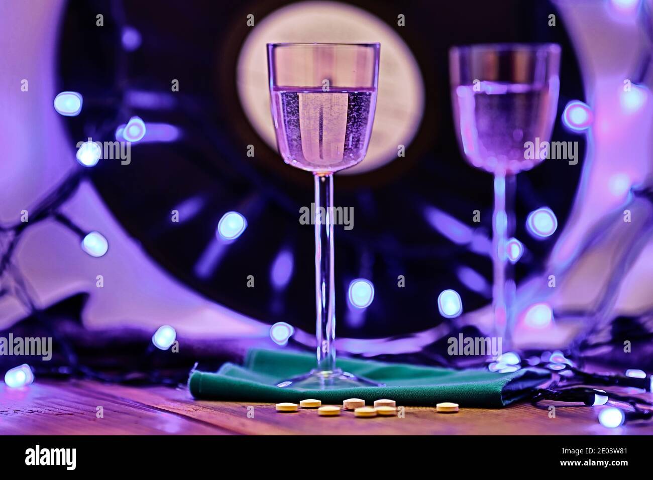 Soft Focus Foto von zwei Gläsern Champagner und Pillen auf dem Hintergrund einer Vinyl-Platte, umgeben von hellen Club Beleuchtung Stockfoto