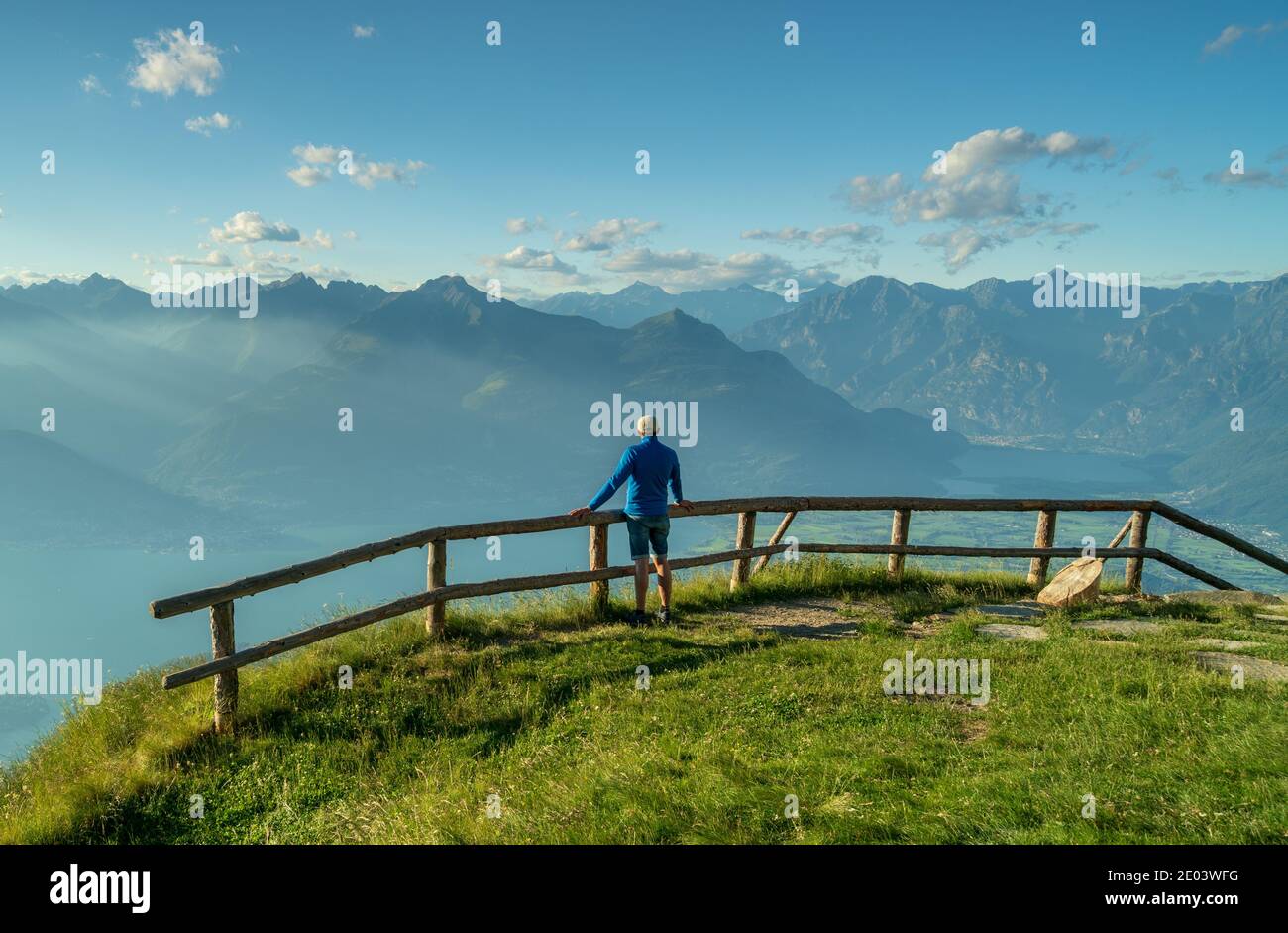 Person von hinten mit blauem Dressing, das auf einem hölzernen lehnt Zaun mit Blick auf die Berge Stockfoto