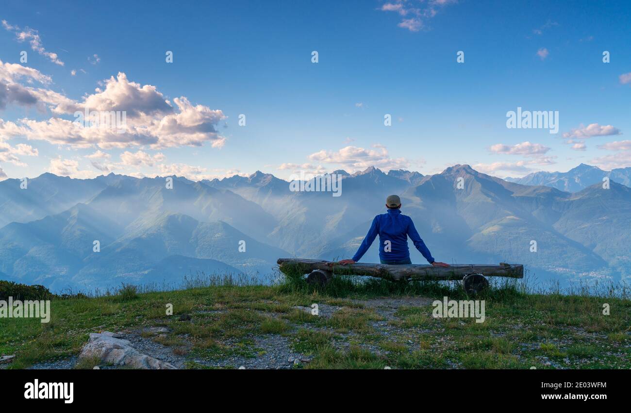 Person von hinten auf einer Holzbank sitzend und anblickend Weite offene Aussicht mit Bergen am Horizont Stockfoto