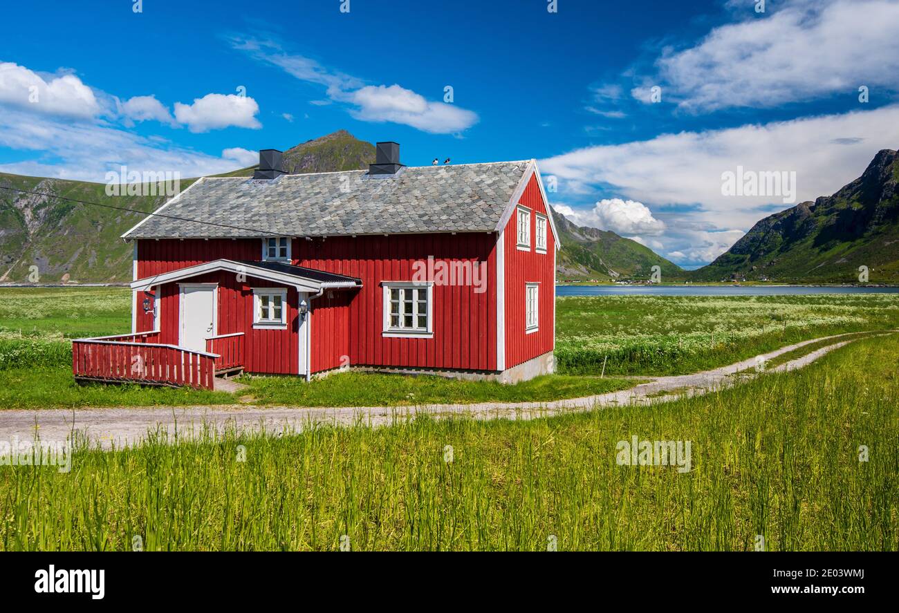 Vaeroy Island Lofoten Islands Nordland Norwegen Rotes Haus in grün Wiesen mit blauem Himmel mit weißen Wolken im Sommer in Norwegen Stockfoto