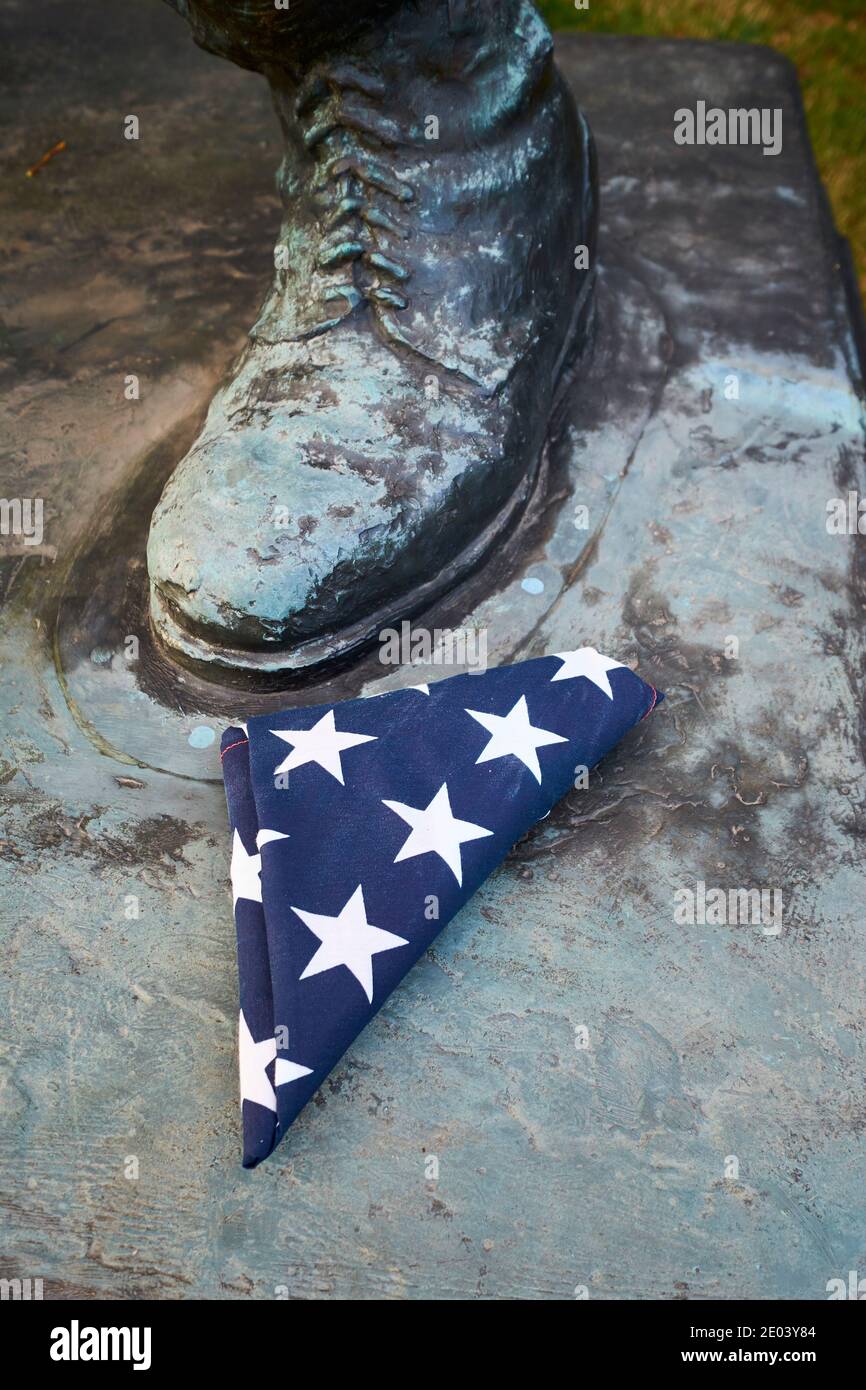 Eine gefaltete amerikanische Flagge sitzt neben dem Fuß einer Bronzeskulptur eines Marinesoldaten. Am SeeBees-Denkmal in der Nähe des Nationalfriedhofs von Arlington in Vir Stockfoto