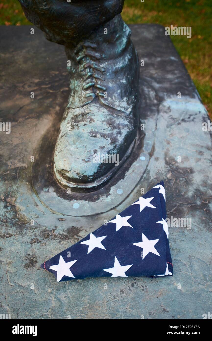 Eine gefaltete amerikanische Flagge sitzt neben dem Fuß einer Bronzeskulptur eines Marinesoldaten. Am SeeBees-Denkmal in der Nähe des Nationalfriedhofs von Arlington in Vir Stockfoto