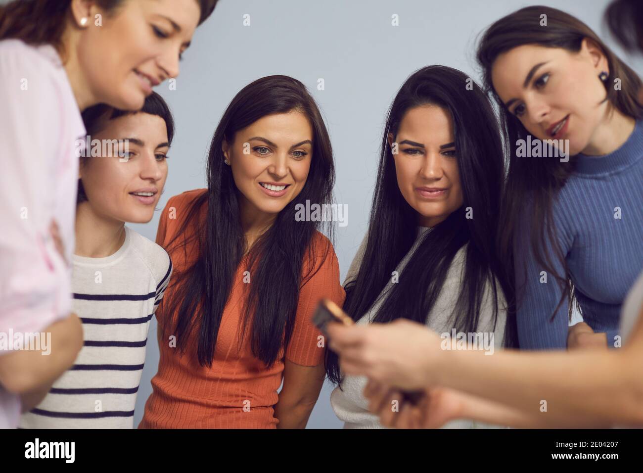 Freundinnen in lässiger Kleidung stehen zusammen im Kreis und Smartphone betrachten Stockfoto