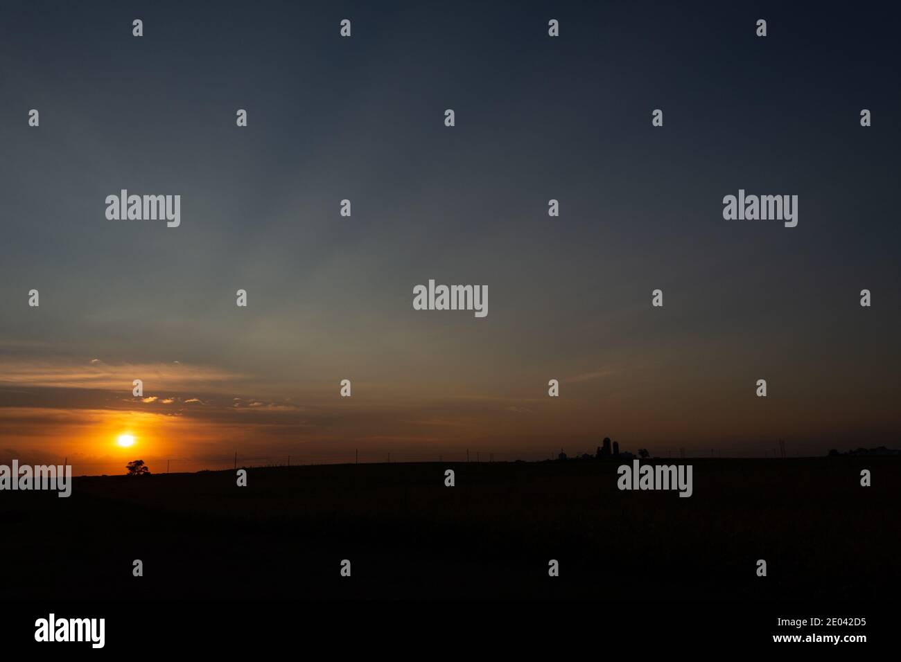 Eine untergehende Sonne umraunt den Horizont und entfernte Farmsilos in Ankeny, Iowa. Stockfoto