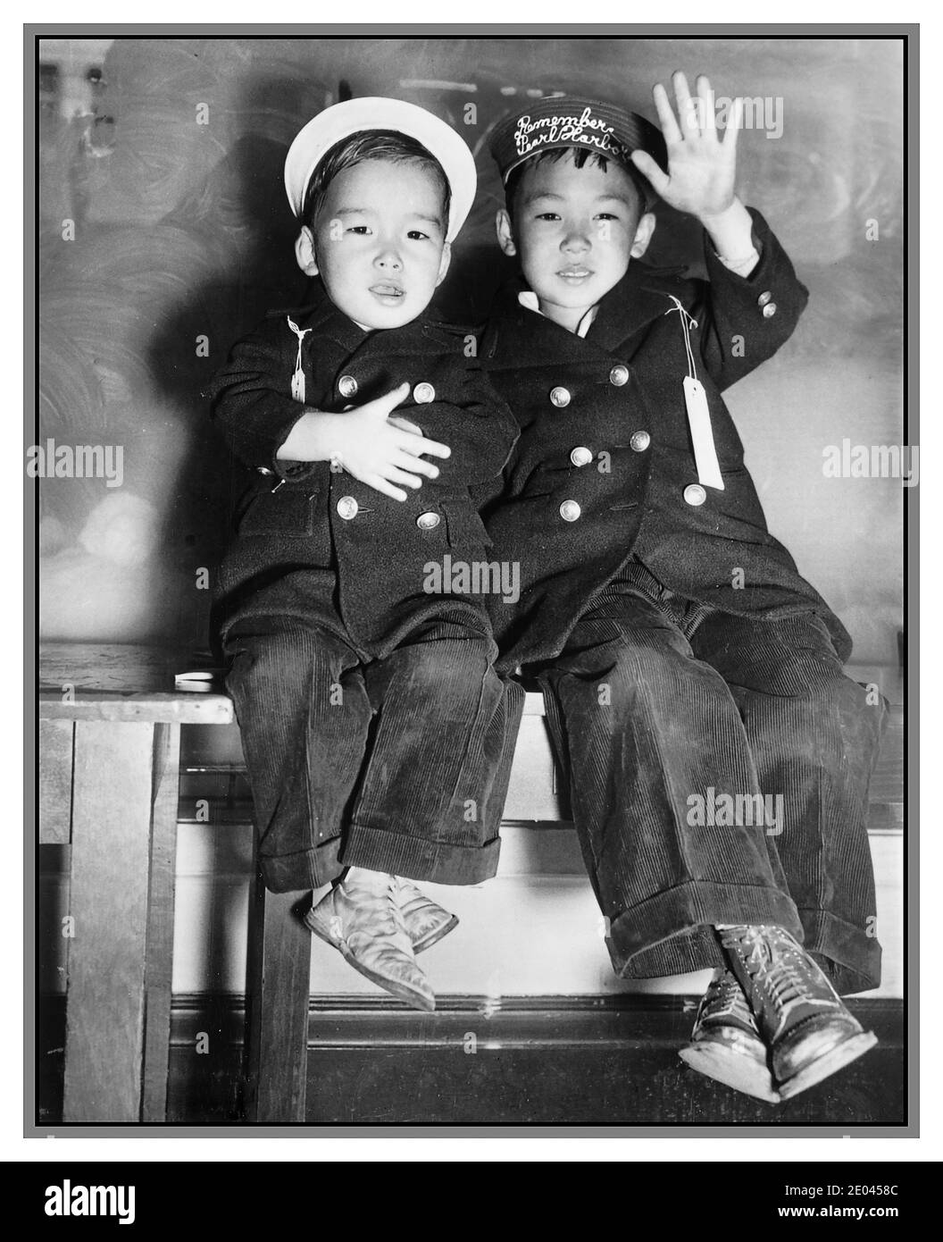 Propagandafoto des 2. Weltkrieges Japanische Evakuierung aus den USA San Francisco (Kalifornien) 1941 Evakuierung - zwei japanische Jungen, einer mit Streifen 'Remember Pearl Harbor' auf dem Hut, winken Abschied [während] warten auf den Bus USA. Armee. Signal Corps.[1942] - Evakuierungen--Kalifornien--San Francisco-1940-1950 - Jungen--Kalifornien--San Francisco-1940-1950 - Weltkrieg, 1939-1945--Japanische Amerikaner--Kalifornien--San Francisco Ankunft und Abreise--Kalifornien--San Francisco-1940-1950 Fotodrucke--1940-1950. Stockfoto