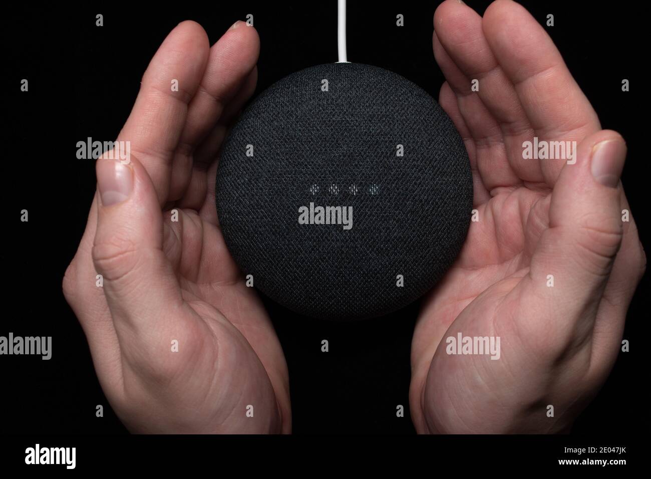 London, Vereinigtes Königreich - 19. Dezember 2020: Hände um einen Google Nest Home Mini Smart Speaker mit eingebautem Google Assistant auf schwarzem Hintergrund. Stockfoto