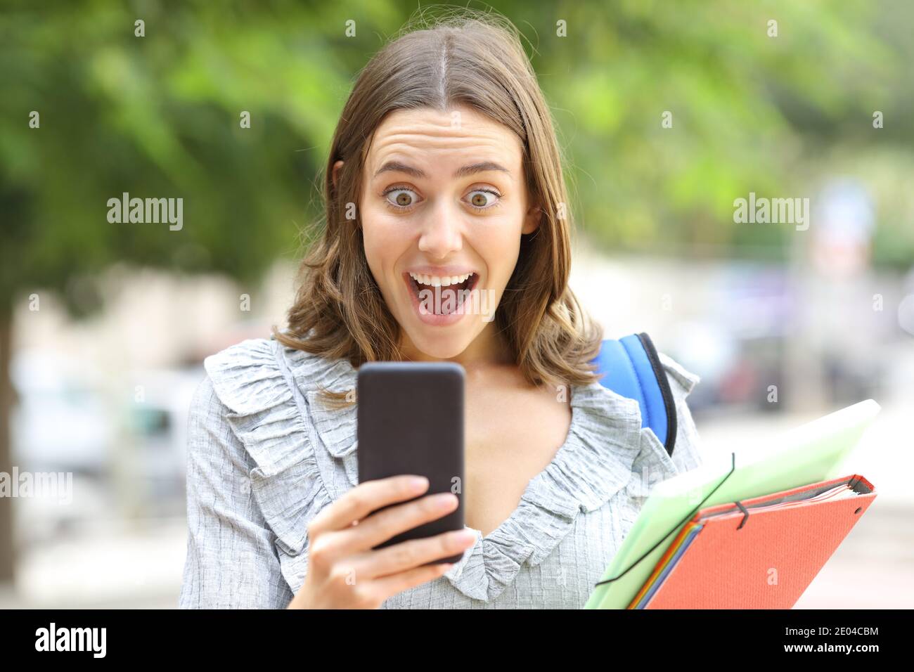 Vorderansicht eines staunenden Studenten, der Nachrichten über Smartphones nachlesen kann Zu Fuß auf der Straße Stockfoto