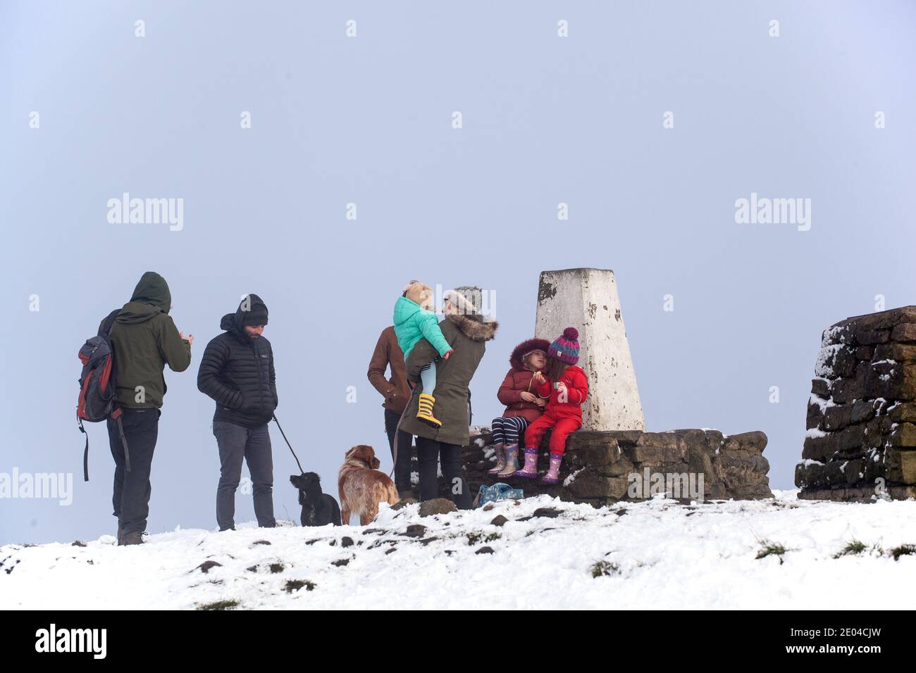 Familie mit Kindern und Hunden am trig Point or Triangulationspunkt auf dem Gipfel der Bosley Cloud bei Congleton Cheshire im Winterschnee Stockfoto