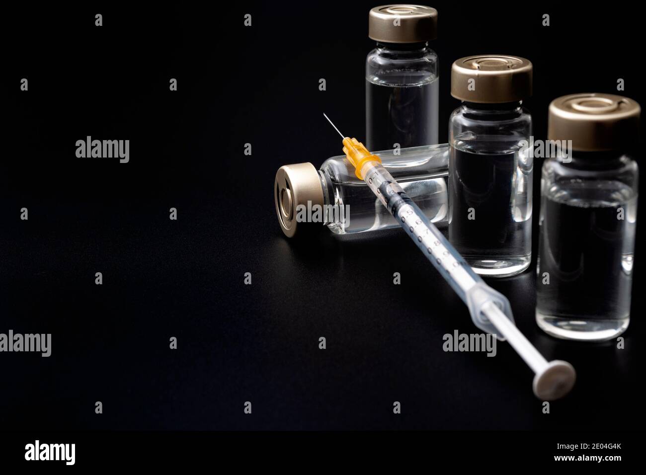 Impfstoffe, Botulinumtoxin und Insulinampullen – Konzeptthema mit Glasfläschchen mit klarer Flüssigkeit neben einer Spritze und einer auf b isolierten hypodermischen Nadel Stockfoto