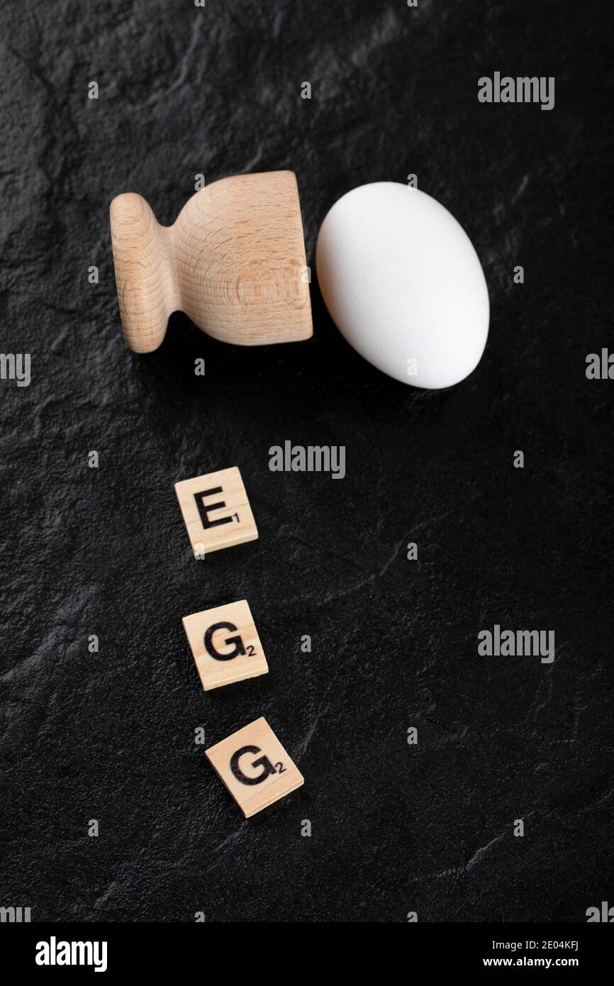 Einzelnes Ei und Holzbuchstabe geschrieben als Ei auf schwarz Hintergrund Stockfoto