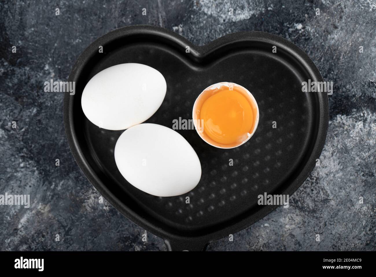 Zwei weiße Eier und Eigelb auf einer herzförmigen Pfanne Stockfoto