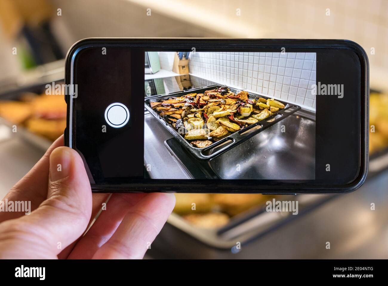 Männliche Hand hat ein Foto von gebratenem Gemüse im Ofen gemacht Tablett zu Hause Stockfoto