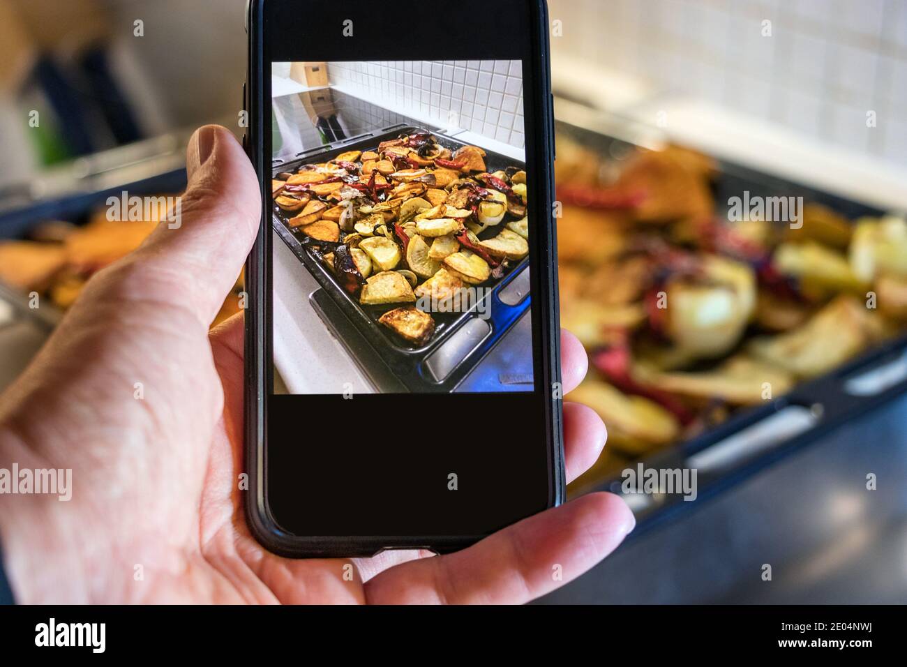 Männliche Hand hat ein Foto von gebratenem Gemüse im Ofen gemacht Tablett zu Hause Stockfoto