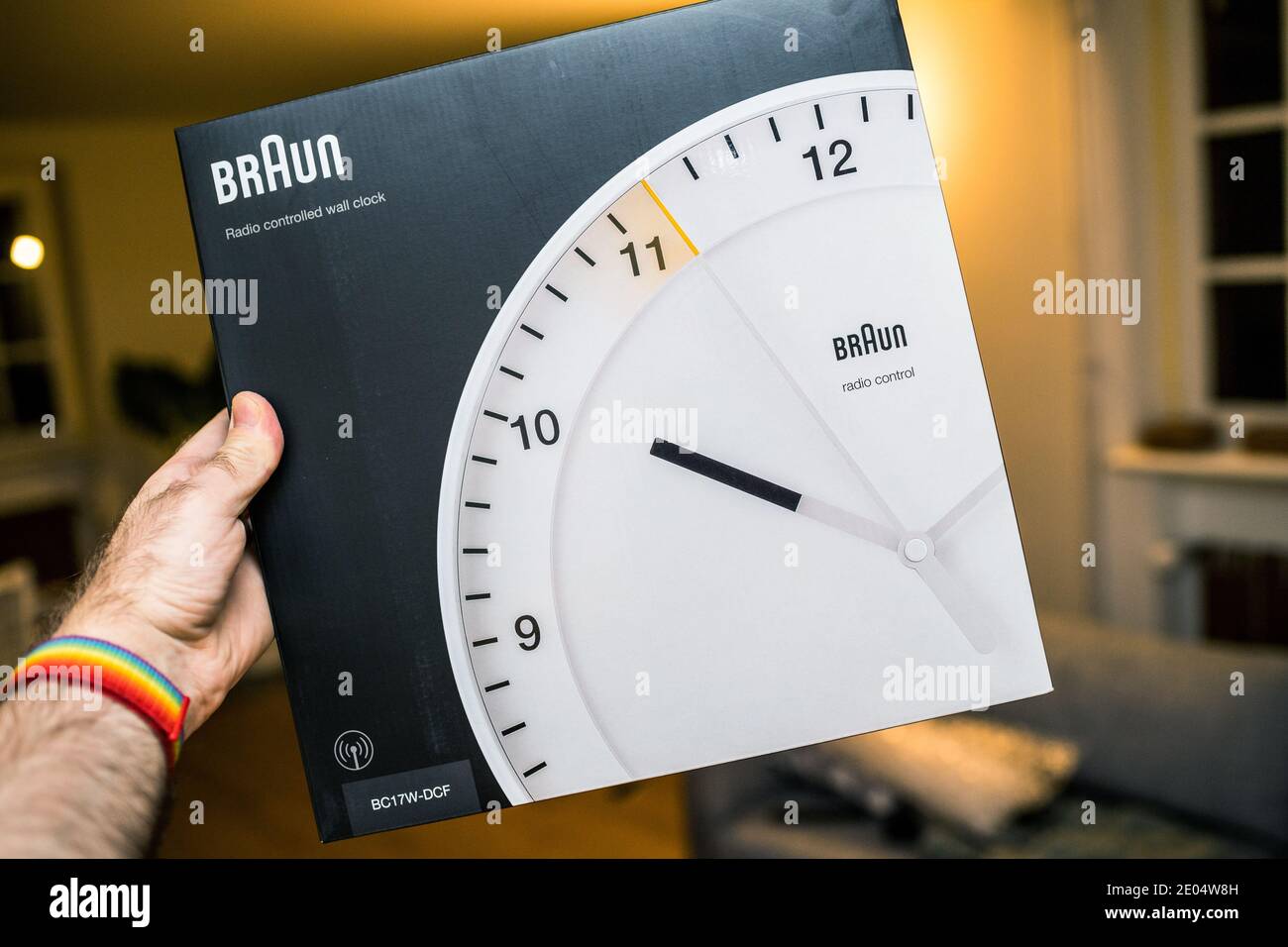 Paris, Frankreich - 8. Dezember 2020: POV persönliche Perspektive männliche Handhaltepaket der neuen Braun BC17F-DCF- Funkuhr traditionelle deutsche Design von Dieter Rams - Wohnzimmer Hintergrund Stockfoto