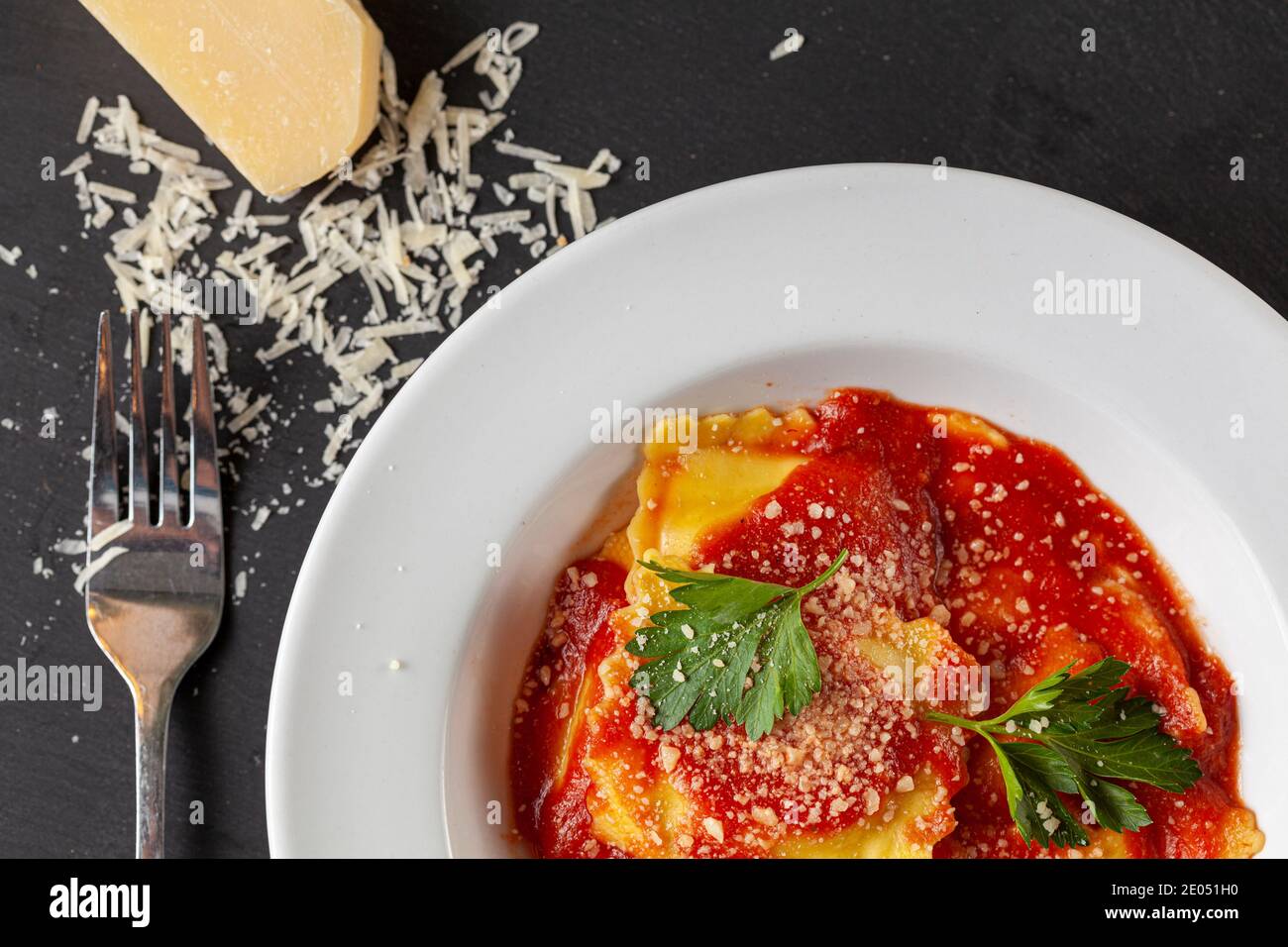 Flaches Bild von weißem Porzellan Teller von italienischen Ravioli in Tomatensauce mit geriebenem Parmesan-Käse und frischen grünen Petersilienblättern beendet. Ein Chee Stockfoto