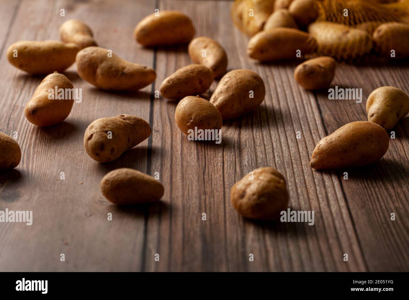 Flache Schärfentiefe dunkles Bild von kleinen unregelmäßig geformten ratte Kartoffeln auf der Oberfläche eines Holztisches aus einem umgekippten Netzsack verstreut. Ein Stockfoto