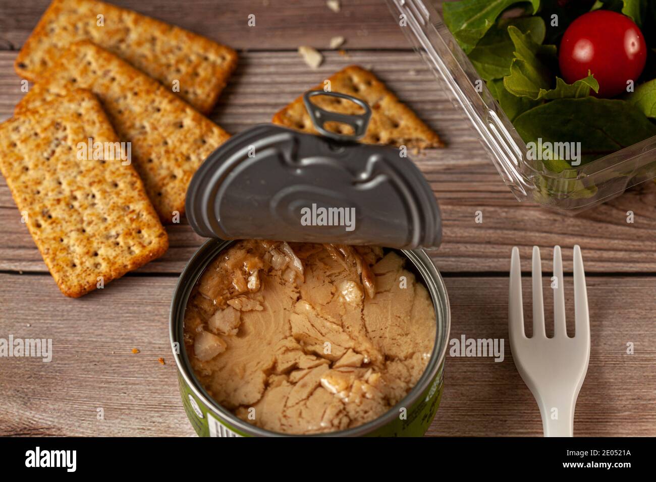 Abgewinkelte Bild von schnell-und Snack-Foto mit einer leicht offenen Dose Thunfisch mit Thunfisch Stücke in Öl auf Holztisch oder Bank, klare Kunststoffbehälter mit Stockfoto