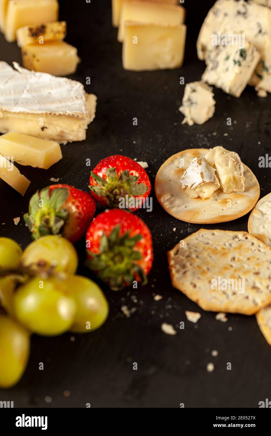 Ein vertikales Bild einer Käseplatte mit einer Auswahl alter französischer, italienischer und Schweizer Käsesortimente auf schwarzem Käseplatte, die serviert werden Stockfoto