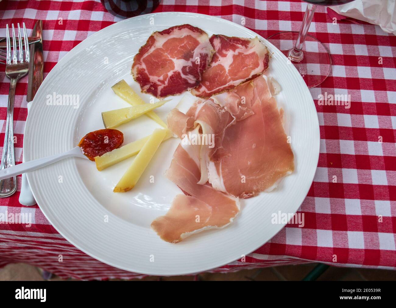 Weißer Teller auf roter und weißer Tischdecke, Käse, Aufschnitt, Snack-Teller für Vorspeisen, Picknick, Prosciutto Stockfoto