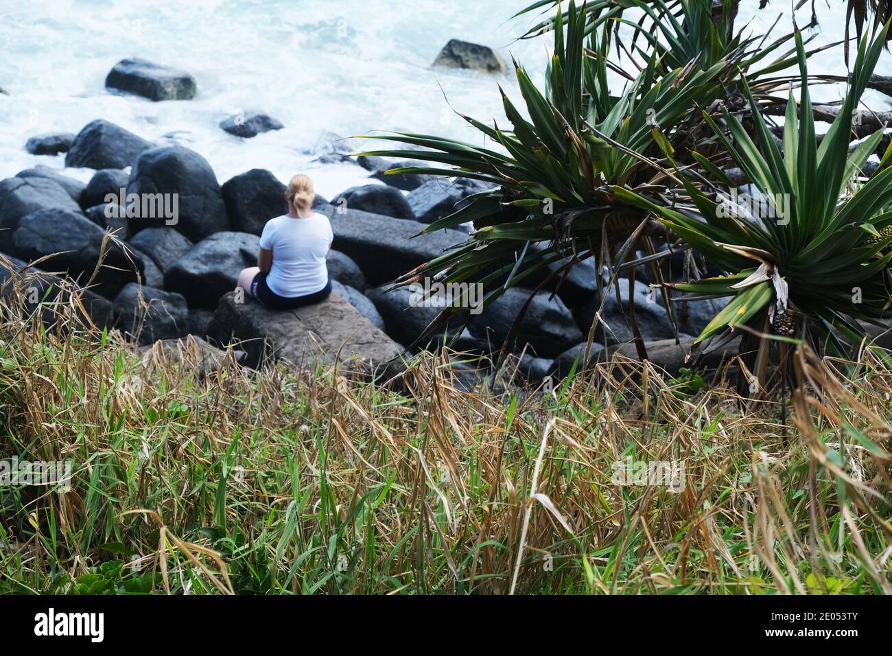 Frau, die auf Felsen sitzt und auf den Ozean blickt Stockfoto