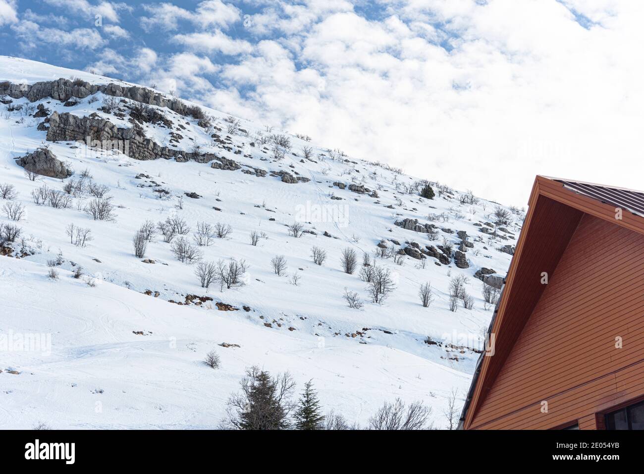 Ein Berg mit flachem Schnee bedeckt. Büsche gucken aus dem Schnee. Wolkiger blauer Himmel. Blockhütte. Wood Lodge. Golan Heights. Mount Hermon. Hochwertige Fotos Stockfoto